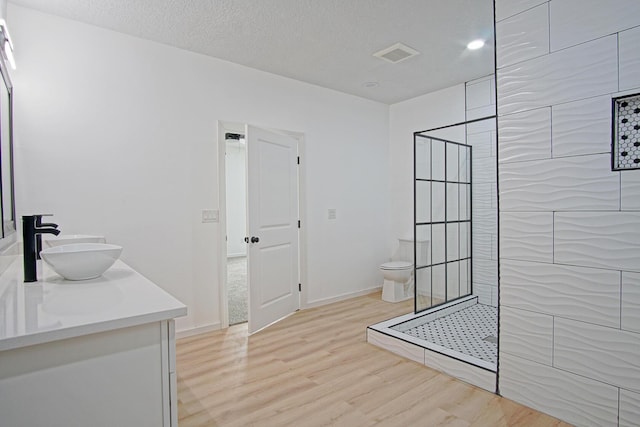 bathroom with tiled shower, toilet, a textured ceiling, vanity, and hardwood / wood-style floors