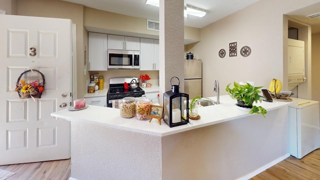 kitchen featuring light hardwood / wood-style floors, white fridge, black gas stove, and kitchen peninsula