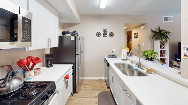 kitchen with white cabinets, appliances with stainless steel finishes, light wood-type flooring, and sink