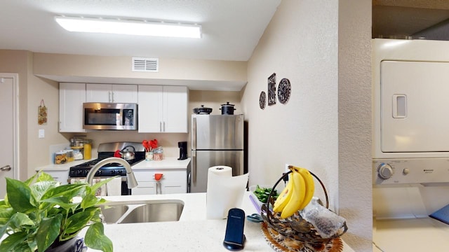 kitchen with white cabinetry, stacked washer and dryer, stainless steel appliances, and sink