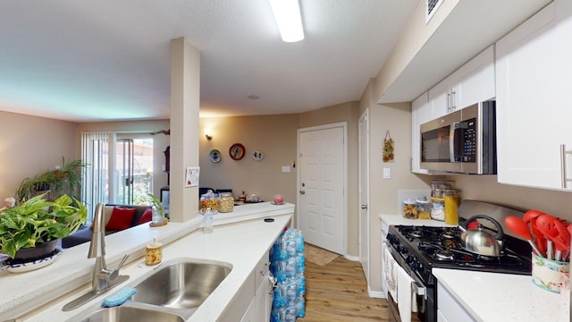 kitchen featuring gas stove, light hardwood / wood-style floors, white cabinetry, and sink