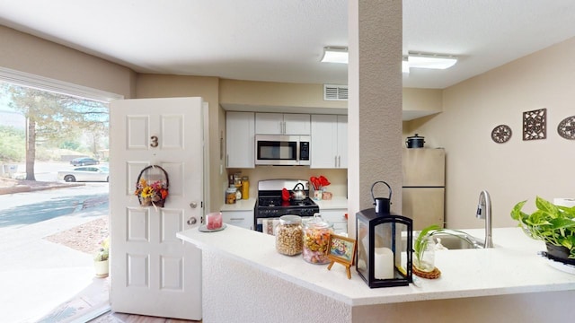 kitchen featuring kitchen peninsula, sink, white cabinets, black gas stove, and fridge