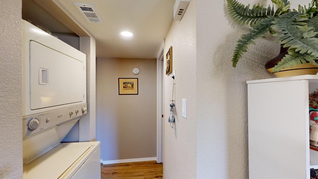 laundry area with light hardwood / wood-style floors and stacked washing maching and dryer