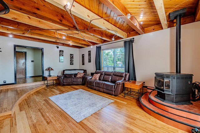 living room featuring beamed ceiling, wooden ceiling, a wood stove, and hardwood / wood-style floors