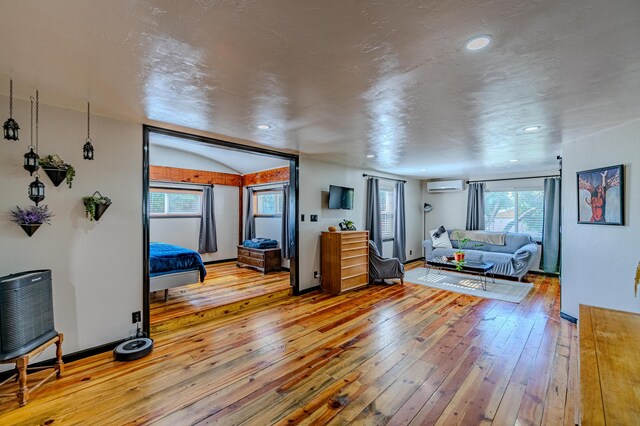 living room with plenty of natural light, hardwood / wood-style flooring, an AC wall unit, and lofted ceiling