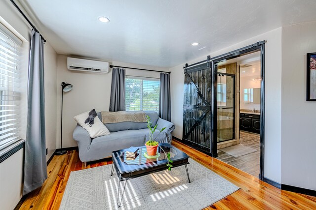 living room with a barn door, a wall unit AC, and wood-type flooring