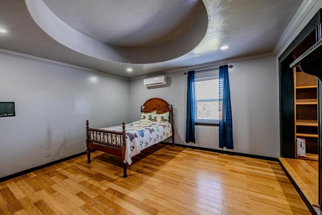 bedroom featuring an AC wall unit, ornamental molding, light hardwood / wood-style flooring, and a raised ceiling