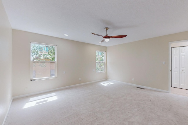 spare room with light colored carpet, a wealth of natural light, and ceiling fan