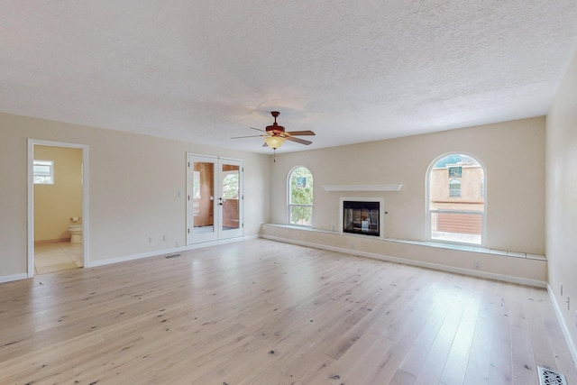 unfurnished living room featuring ceiling fan, french doors, a textured ceiling, and light wood-type flooring