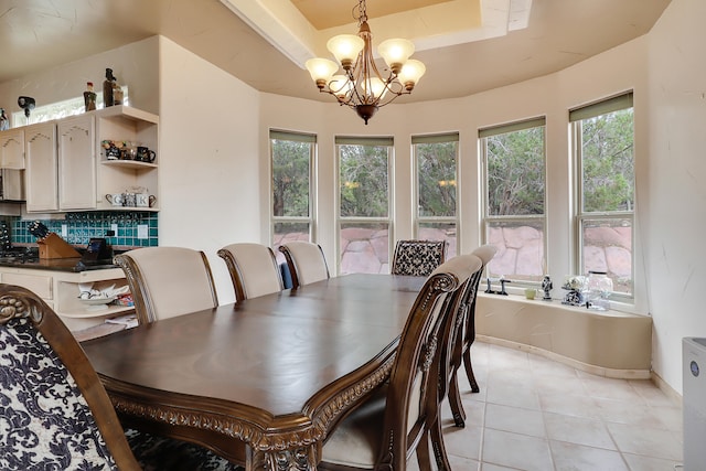 tiled dining room with an inviting chandelier, a raised ceiling, and a healthy amount of sunlight