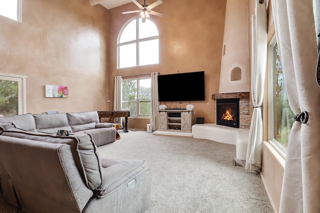 living room with ceiling fan, carpet flooring, a fireplace, and a high ceiling