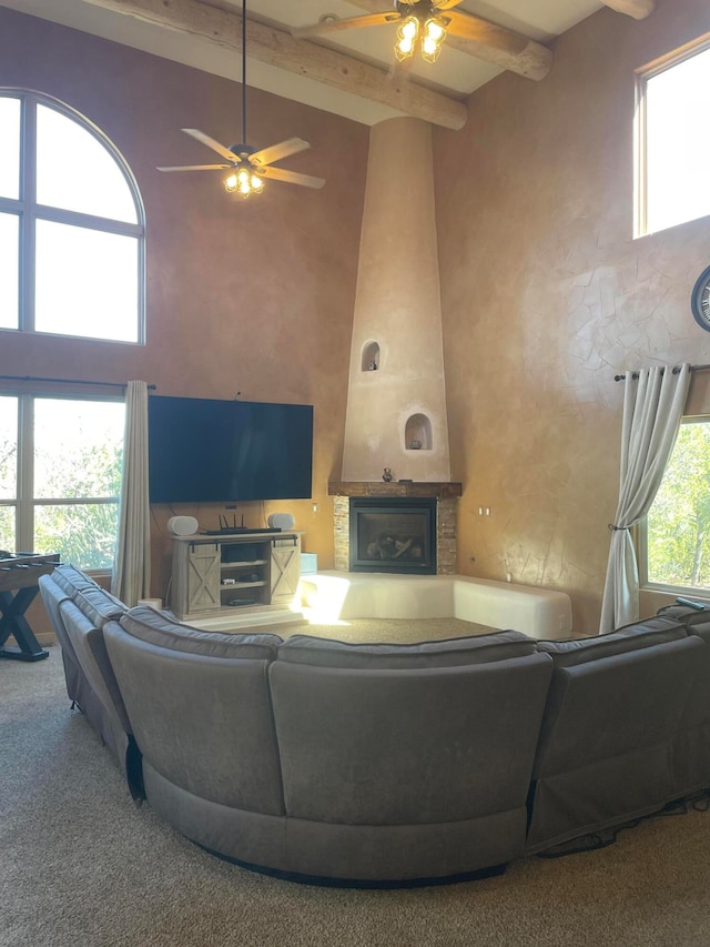 living room featuring high vaulted ceiling, carpet floors, a fireplace, beamed ceiling, and ceiling fan