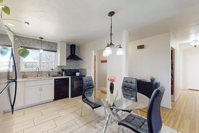 kitchen featuring sink, white cabinets, wall chimney exhaust hood, hanging light fixtures, and black appliances