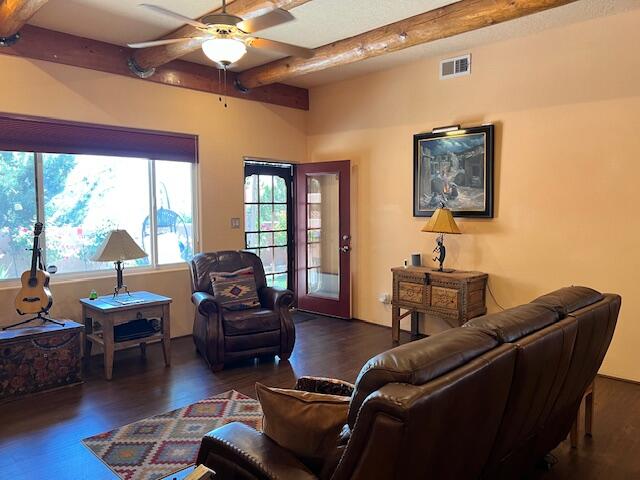 living room featuring dark wood-type flooring, ceiling fan, and beam ceiling