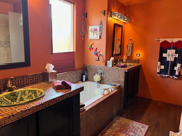 bathroom featuring wood-type flooring, large vanity, tiled tub, and double sink