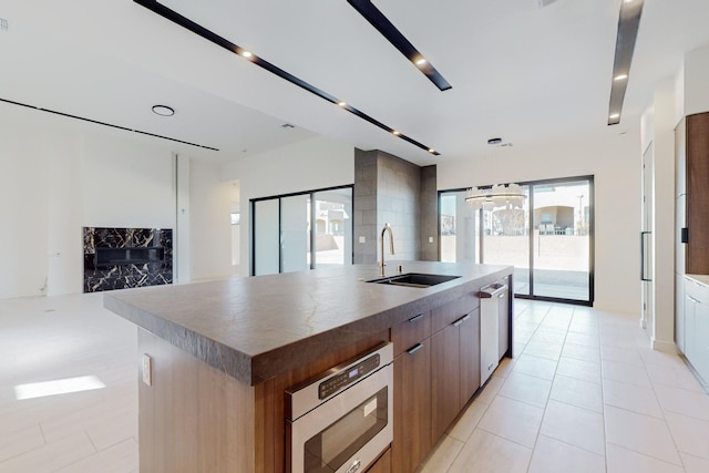 kitchen with sink, a premium fireplace, appliances with stainless steel finishes, light tile patterned flooring, and a large island with sink