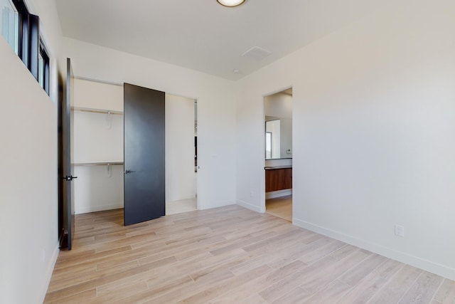 unfurnished bedroom with ensuite bath, a closet, and light wood-type flooring