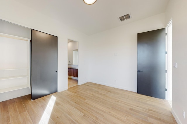 unfurnished bedroom featuring a closet, connected bathroom, and light hardwood / wood-style flooring