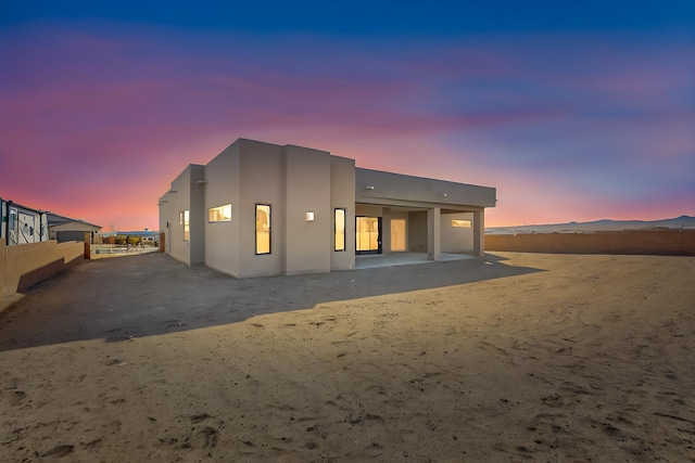 back house at dusk featuring a mountain view and a patio area