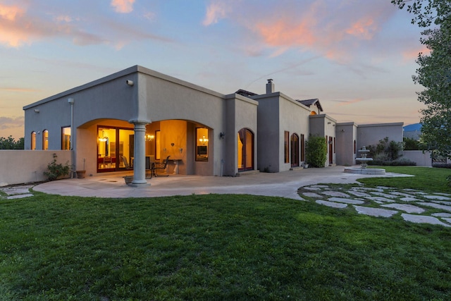 back house at dusk with a patio area and a lawn