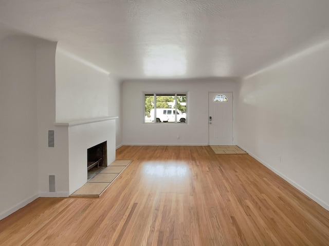 unfurnished living room featuring light wood-type flooring and a tiled fireplace