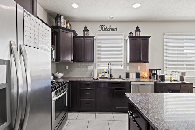 kitchen featuring dark brown cabinetry, sink, tasteful backsplash, dark stone countertops, and appliances with stainless steel finishes