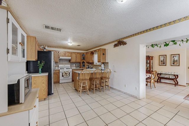 kitchen with kitchen peninsula, a textured ceiling, a breakfast bar, light tile patterned floors, and appliances with stainless steel finishes