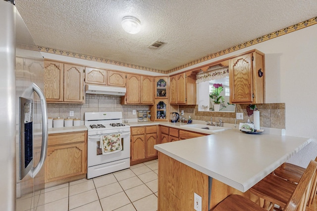 kitchen featuring sink, kitchen peninsula, stainless steel fridge, a breakfast bar, and white gas range oven