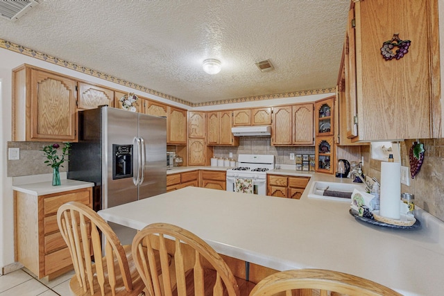 kitchen featuring kitchen peninsula, stainless steel fridge, sink, light tile patterned floors, and white range with gas stovetop