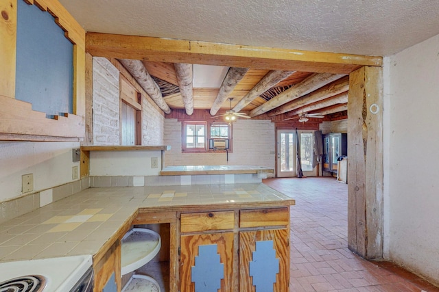 kitchen with beam ceiling, range, a textured ceiling, ceiling fan, and tile countertops