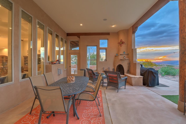 patio terrace at dusk featuring exterior fireplace and a grill