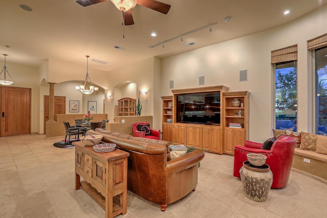 carpeted living room with track lighting, ceiling fan with notable chandelier, and ornate columns