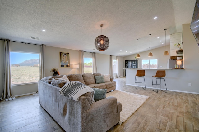 living room featuring light hardwood / wood-style floors, a textured ceiling, lofted ceiling, and plenty of natural light