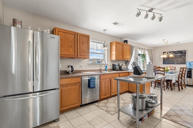 kitchen with a textured ceiling, hanging light fixtures, stainless steel appliances, an inviting chandelier, and sink