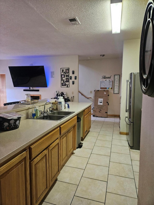 kitchen featuring a textured ceiling, light tile patterned flooring, sink, and stainless steel refrigerator