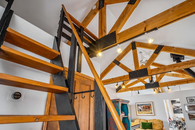 staircase featuring beamed ceiling, rail lighting, and high vaulted ceiling