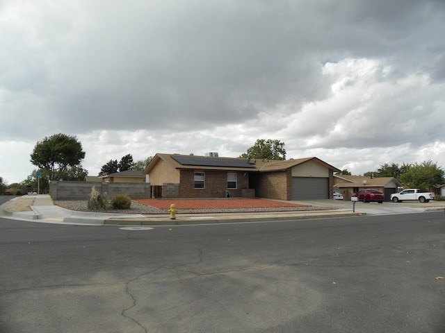 view of front facade with an attached garage, driveway, fence, and solar panels