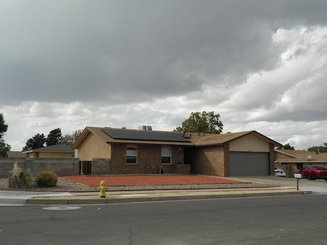 ranch-style home with driveway, an attached garage, brick siding, fence, and roof mounted solar panels