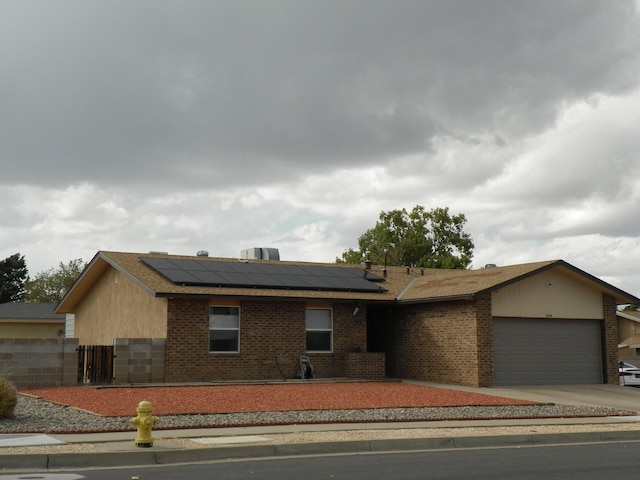 single story home with a garage, solar panels, and brick siding