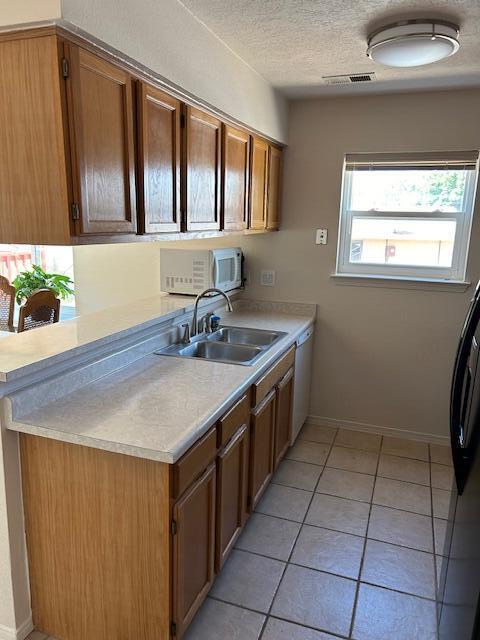 kitchen with light countertops, visible vents, brown cabinetry, dishwasher, and a sink