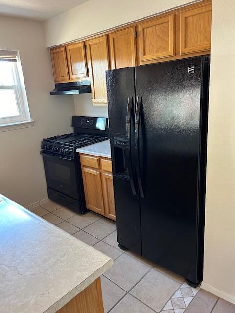 kitchen with brown cabinetry, under cabinet range hood, light countertops, and black appliances