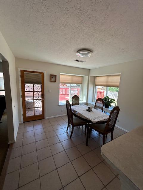 tiled dining room featuring visible vents, a wealth of natural light, baseboards, and a textured ceiling