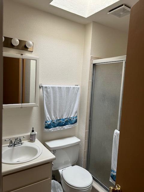 bathroom featuring toilet, vanity, a skylight, and a shower with door