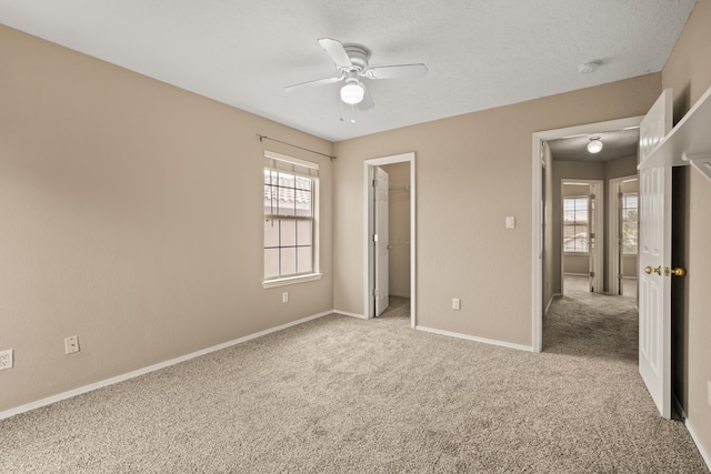 unfurnished bedroom with a closet, a spacious closet, light carpet, and ceiling fan