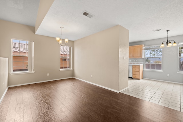 unfurnished room with a textured ceiling, an inviting chandelier, and light hardwood / wood-style flooring