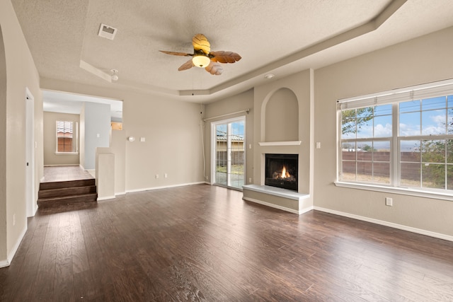 unfurnished living room with a textured ceiling, dark hardwood / wood-style floors, ceiling fan, and a tray ceiling