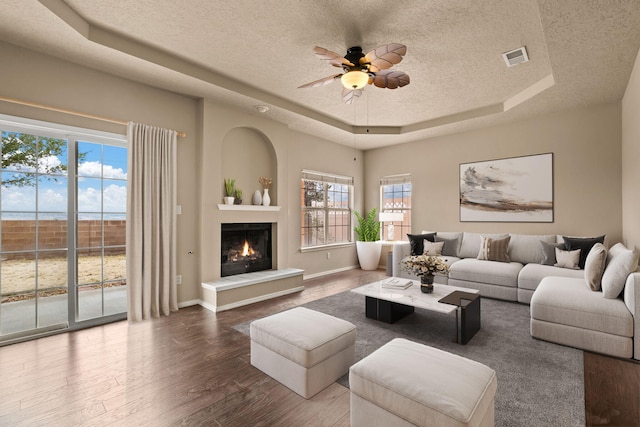 living room with a textured ceiling, wood-type flooring, ceiling fan, and a tray ceiling