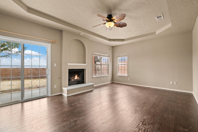 unfurnished living room featuring a textured ceiling, wood-type flooring, ceiling fan, and a raised ceiling