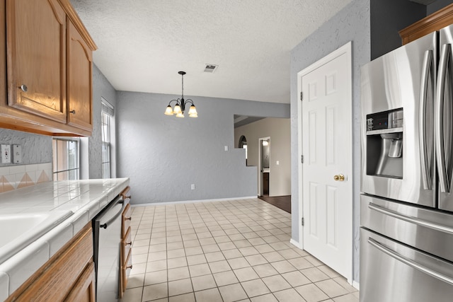 kitchen featuring tile counters, stainless steel appliances, a chandelier, light tile patterned flooring, and pendant lighting