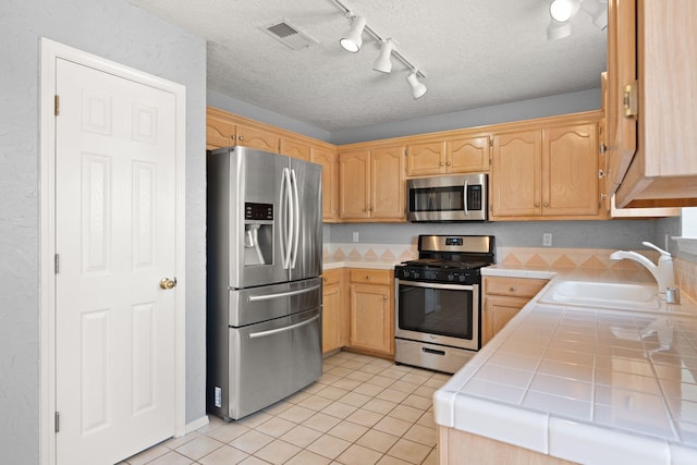 kitchen featuring stainless steel appliances, tile counters, a textured ceiling, and sink